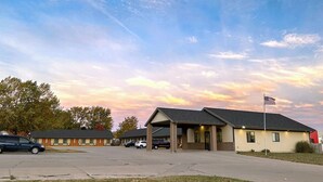 A motel with a covered parking area, a flagpole, and a clear sky with clouds. - Vision Inn Motel (Falls City)