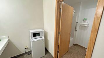 Una habitación pequeña con microondas, refrigerador, una puerta de madera y un perchero con toallas.