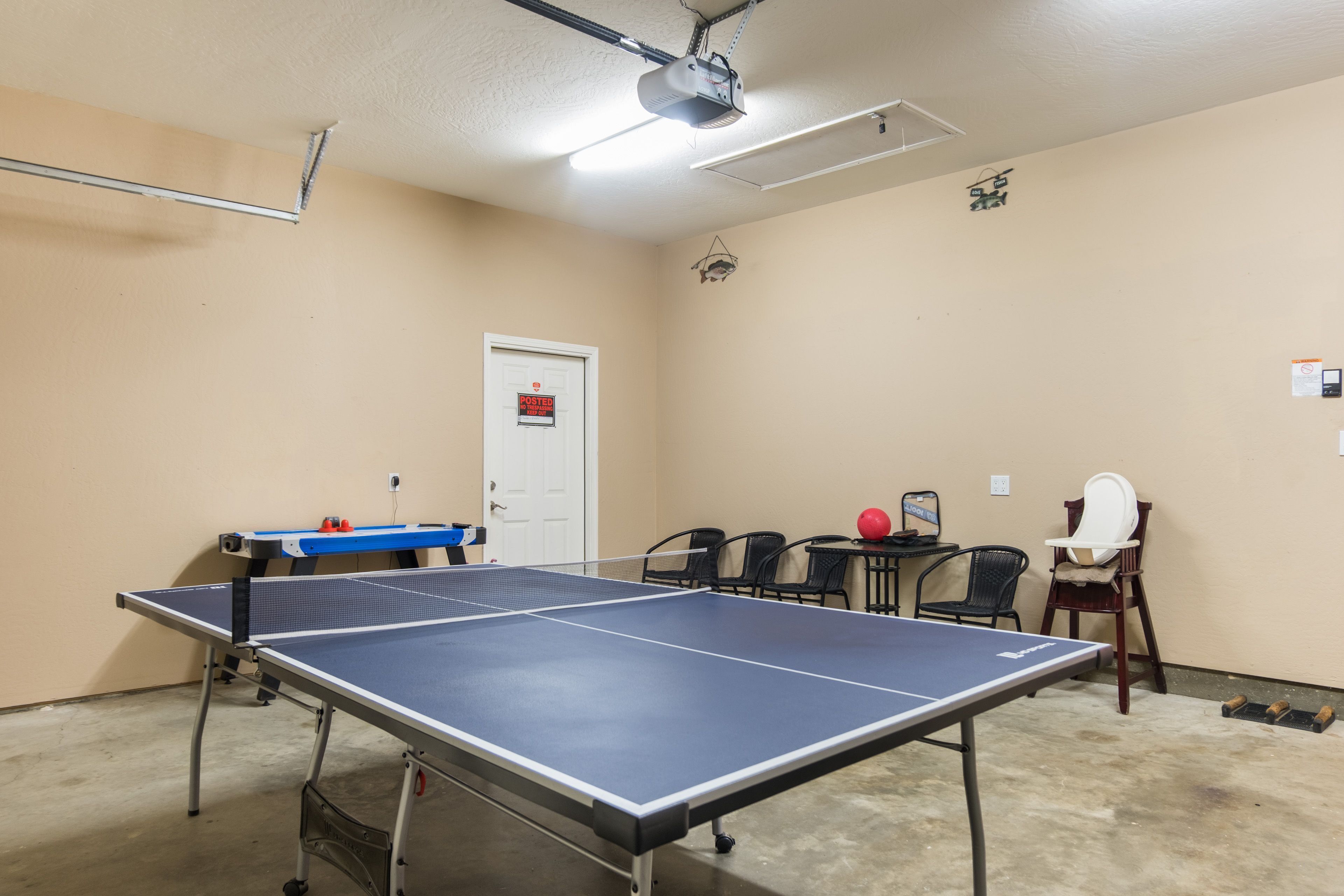 A ping pong table in a room with beige walls, a door, and a projector mounted on the ceiling.