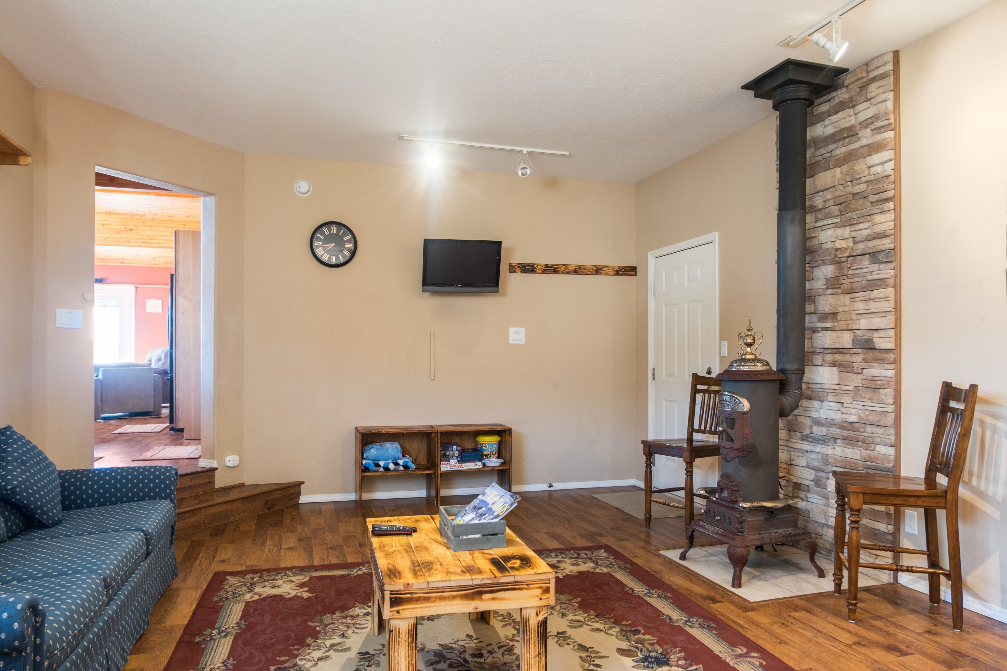 Una sala de estar con sofá, mesa de centro, televisor, chimenea de piedra y una puerta que da a otra habitación.