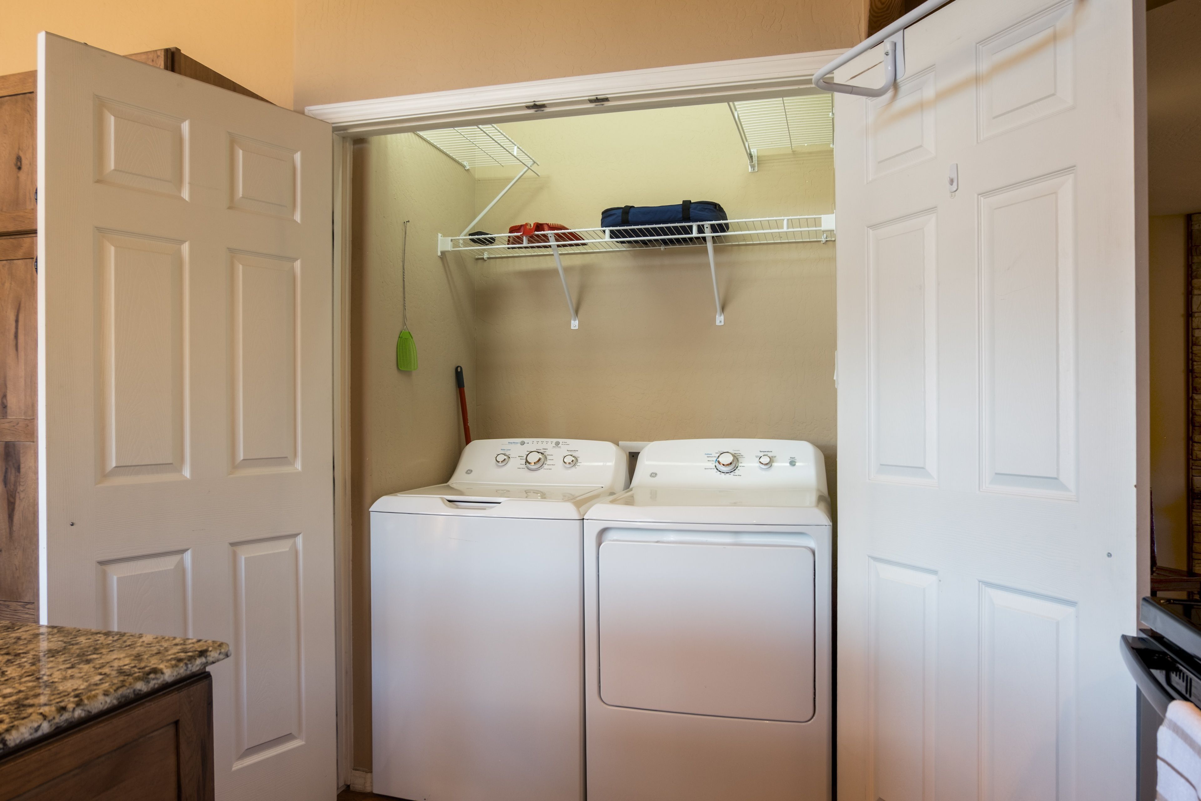 Une buanderie équipée de deux machines à laver et deux sèche-linge superposés, une étagère en métal au-dessus et un plan de travail en bois sur le côté gauche.