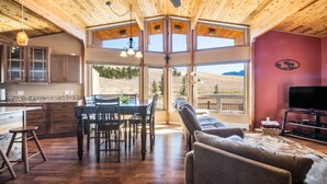 A spacious living area with a wooden ceiling, a dining table with chairs, a sofa, and a television.