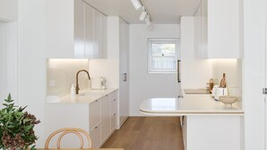 Une cuisine moderne avec des meubles blancs, une table à manger en bois et une fenêtre laissant entrer la lumière naturelle.