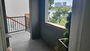 Un balcón con vistas a un lago y edificios, una planta pequeña en maceta y una baranda metálica.