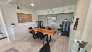 Un comedor con una mesa de madera y sillas negras, una pared gris con obras de arte, un aparador con plantas y una alfombra estampada.