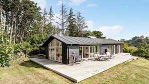 A modern cabin with a deck, large sliding glass doors, and a patio area with outdoor furniture. - Amazing home in Nykøbing Sj with WiFi (Nykøbing Sj)