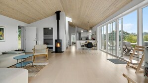 A spacious living area with a central fireplace, a dining area, and large windows offering a view of the outdoors. - Amazing home in Nykøbing Sj with WiFi (Nykøbing Sj)
