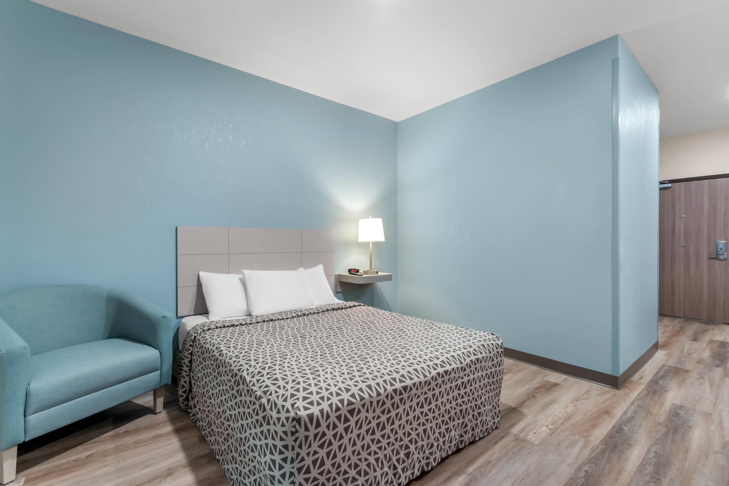 Une chambre à coucher avec un lit, une table de chevet, une lampe, une chaise bleue et une armoire.
