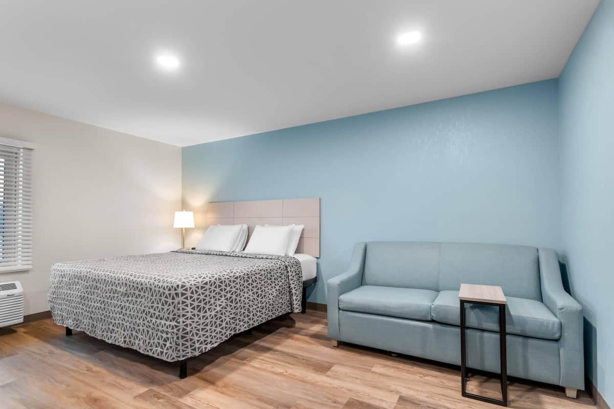 Un dormitorio con cama, mesita de noche, lámpara, sofá y ventana con persianas.