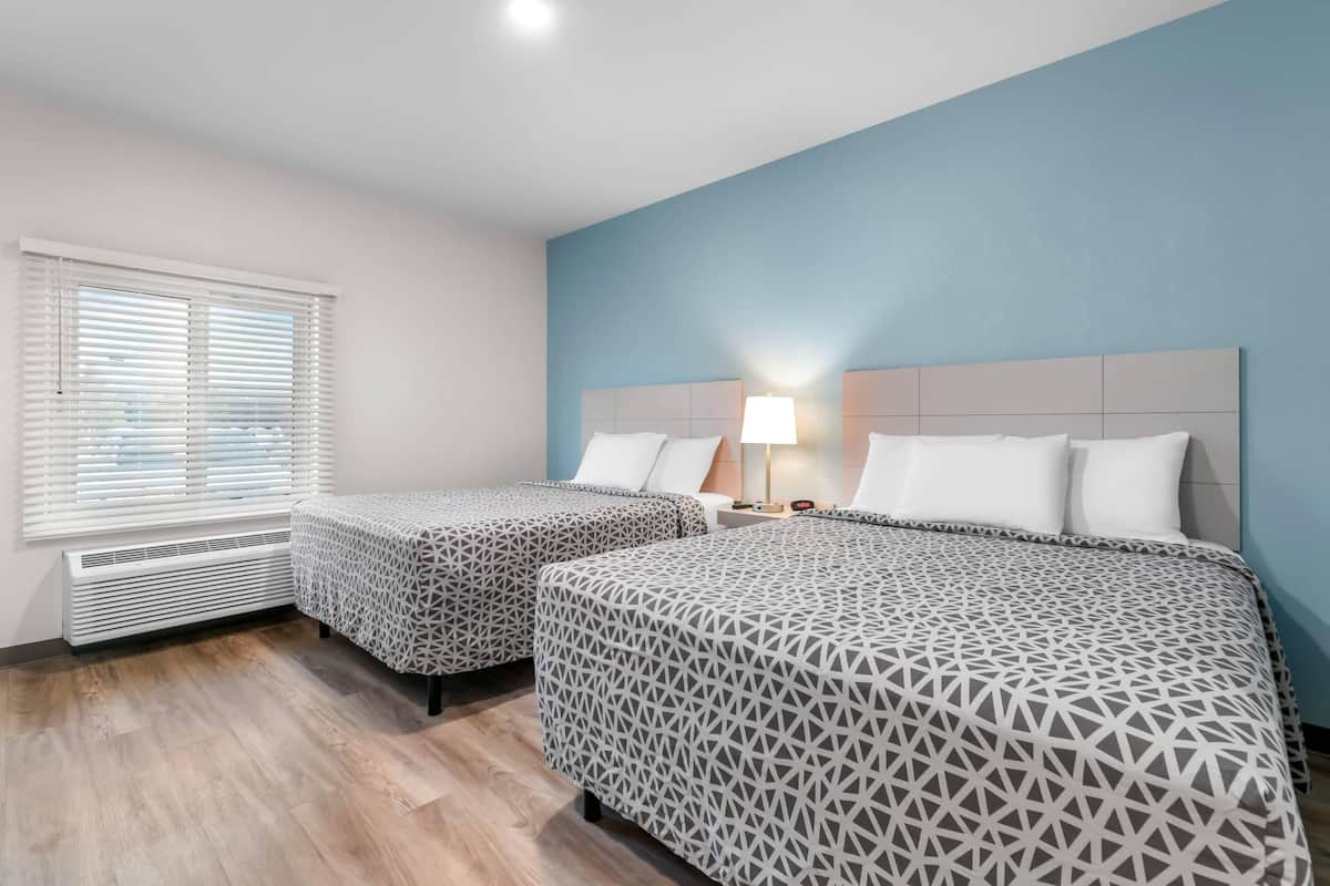 Una habitación de hotel con dos camas, una ventana con persianas, una lámpara de noche y un calentador.