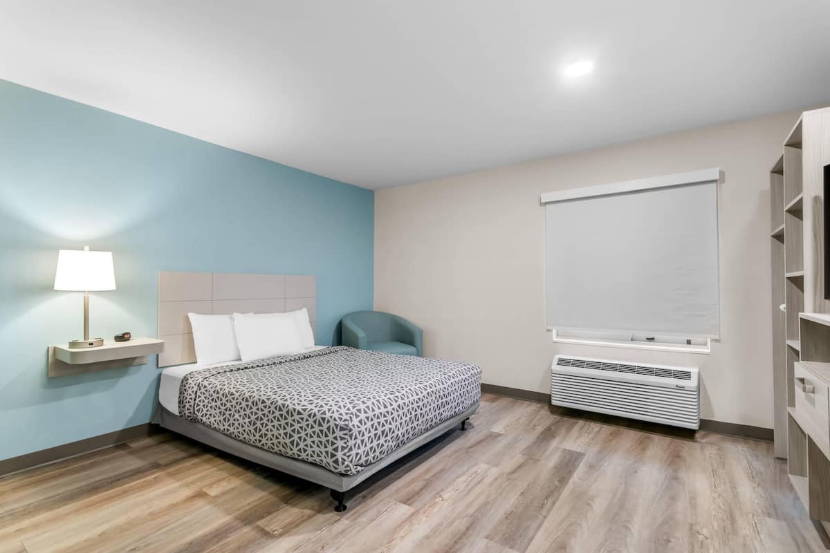 Un dormitorio moderno con una cama, una mesita de noche con lámpara, una silla, un ventanal con persianas y estanterías empotradas.