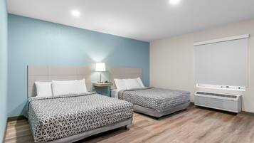Habitación de hotel con dos camas, una mesita de noche con lámpara, una ventana con persianas y un aire acondicionado instalado en la pared.