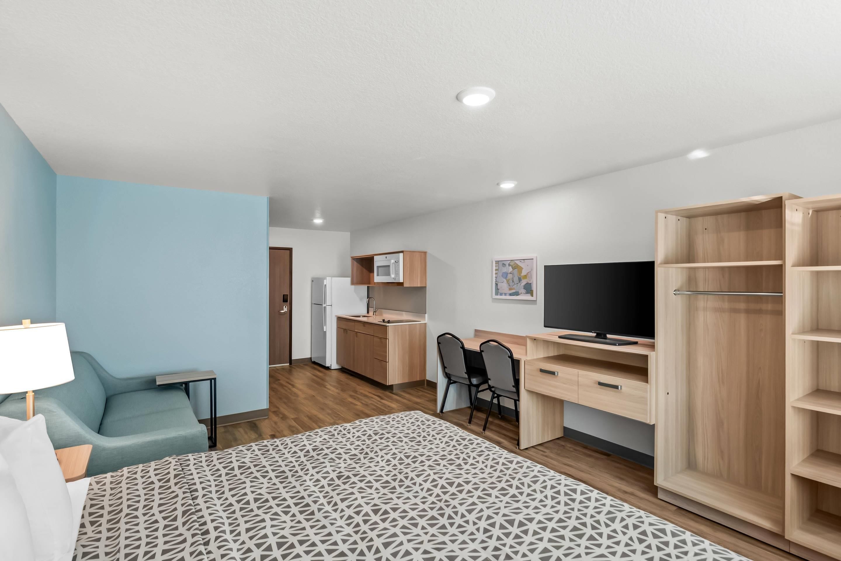 A compact room with a bed, a desk, a chair, a TV, a kitchenette, and a wardrobe.