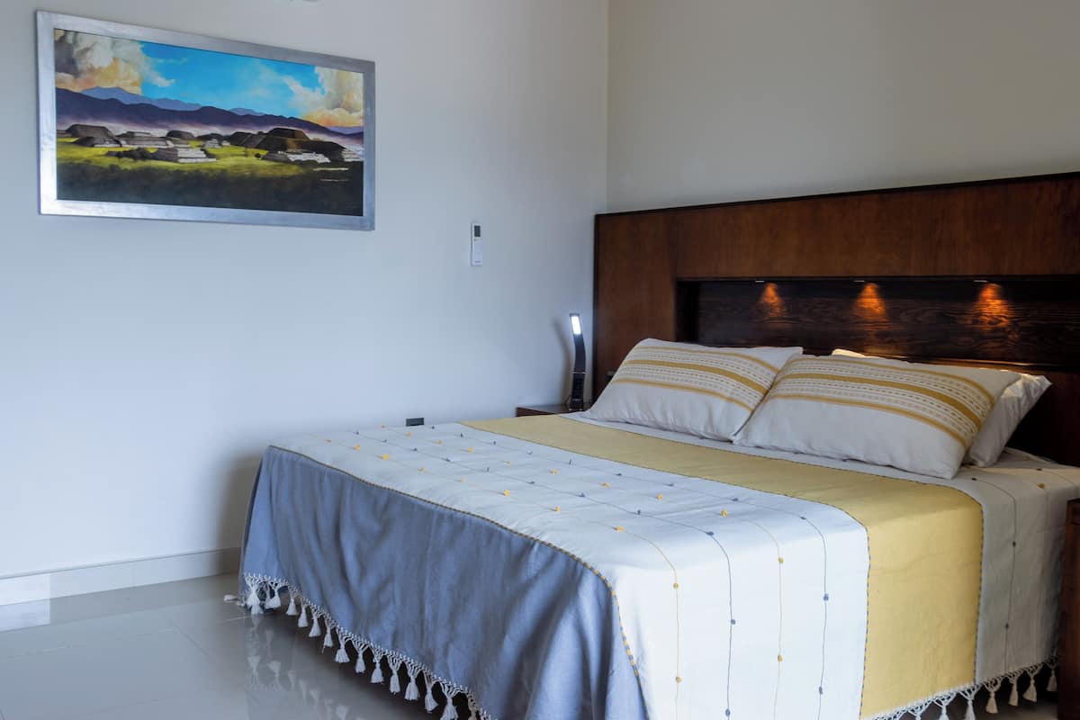 Ein Schlafzimmer mit Bett, Kopfstütze, Nachttisch, Lampe und einem Bild an der Wand.
