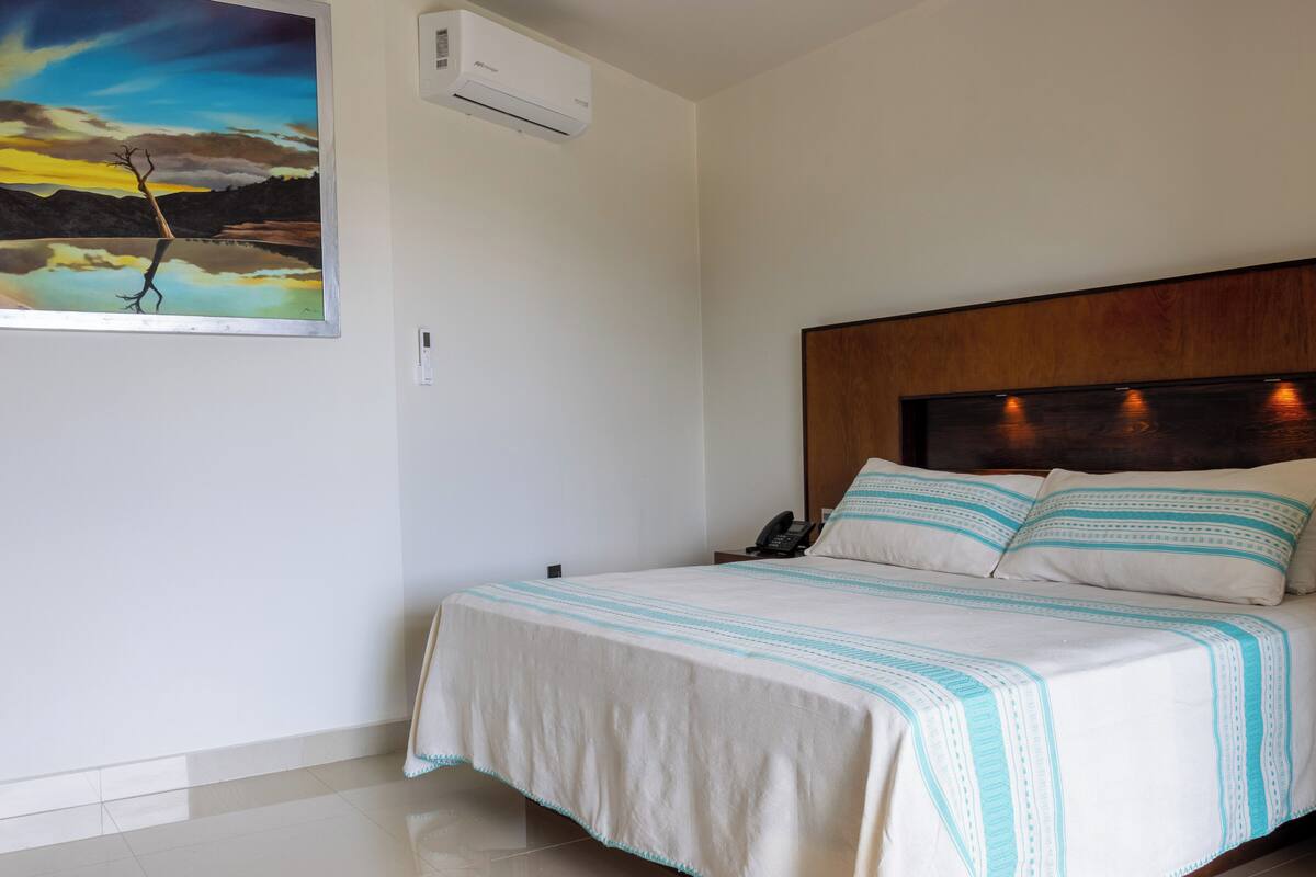 Ein Hotelzimmer mit Bett, einem Bild, einer Klimaanlage, einem Telefon und einem hölzernen Kopfteil.