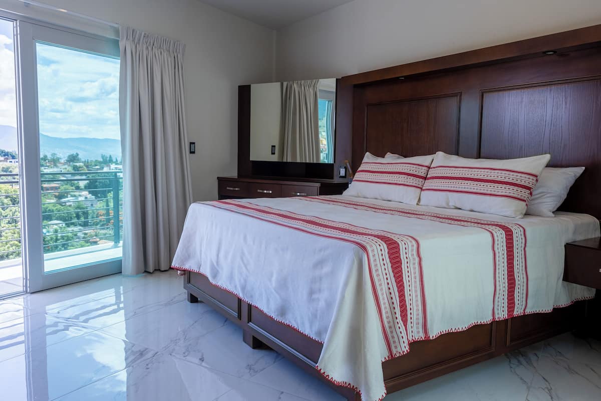 Ein Schlafzimmer mit einem großen Bett, einem hölzernen Kopfteil, einem Spiegel und Blick auf einen Balkon.