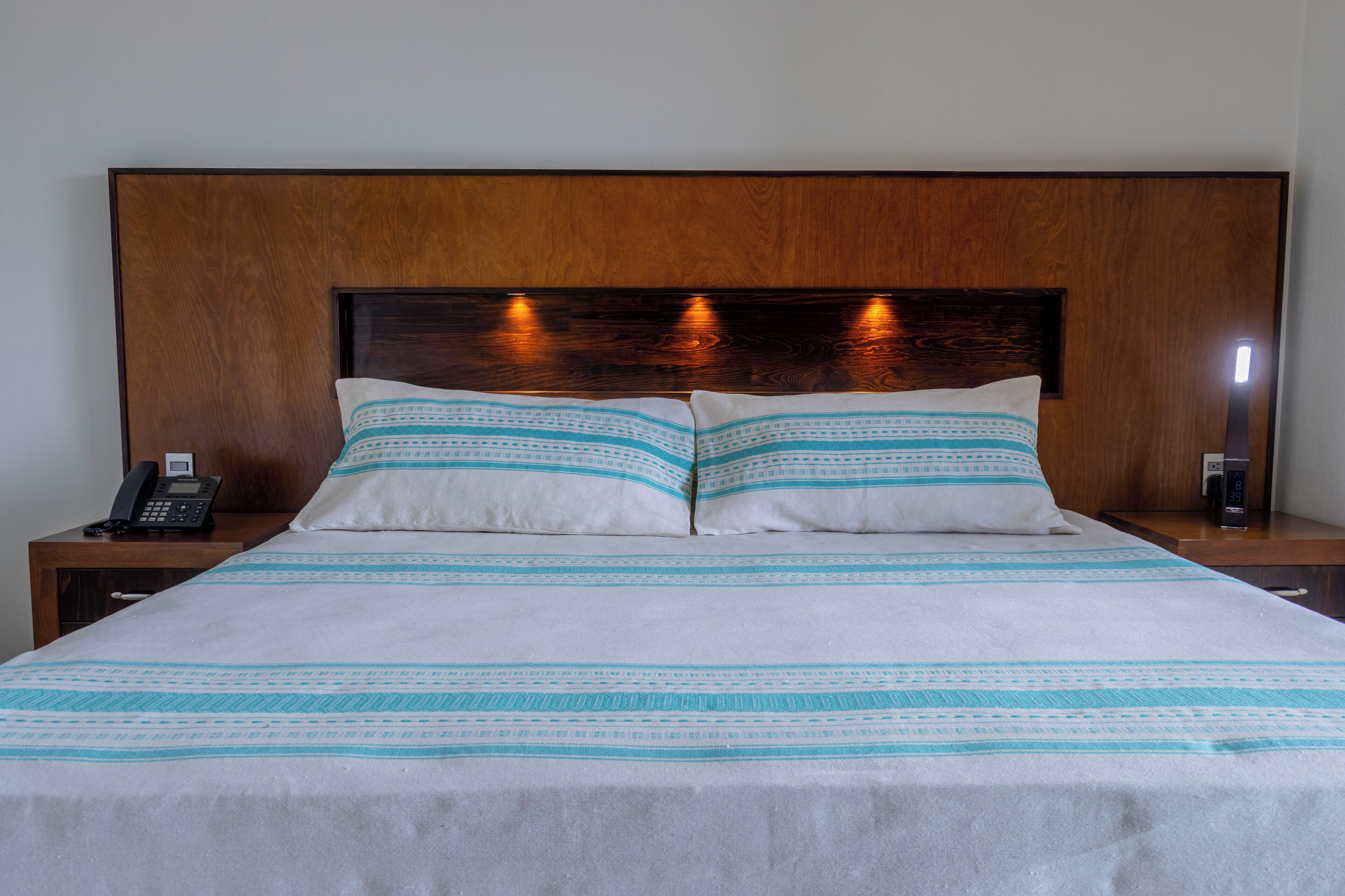 Un letto rifatto con una coperta a righe bianche e azzurre, una testiera in legno e abat-jour.