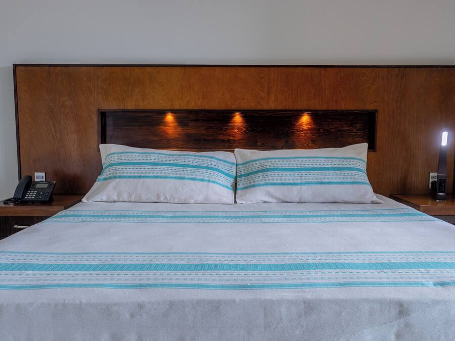 Un letto rifatto con una coperta a righe bianche e azzurre, una testiera in legno e abat-jour.