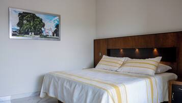 A neatly made bed with a white and yellow striped bedspread, a wooden headboard, and a framed picture of a building on the wall.