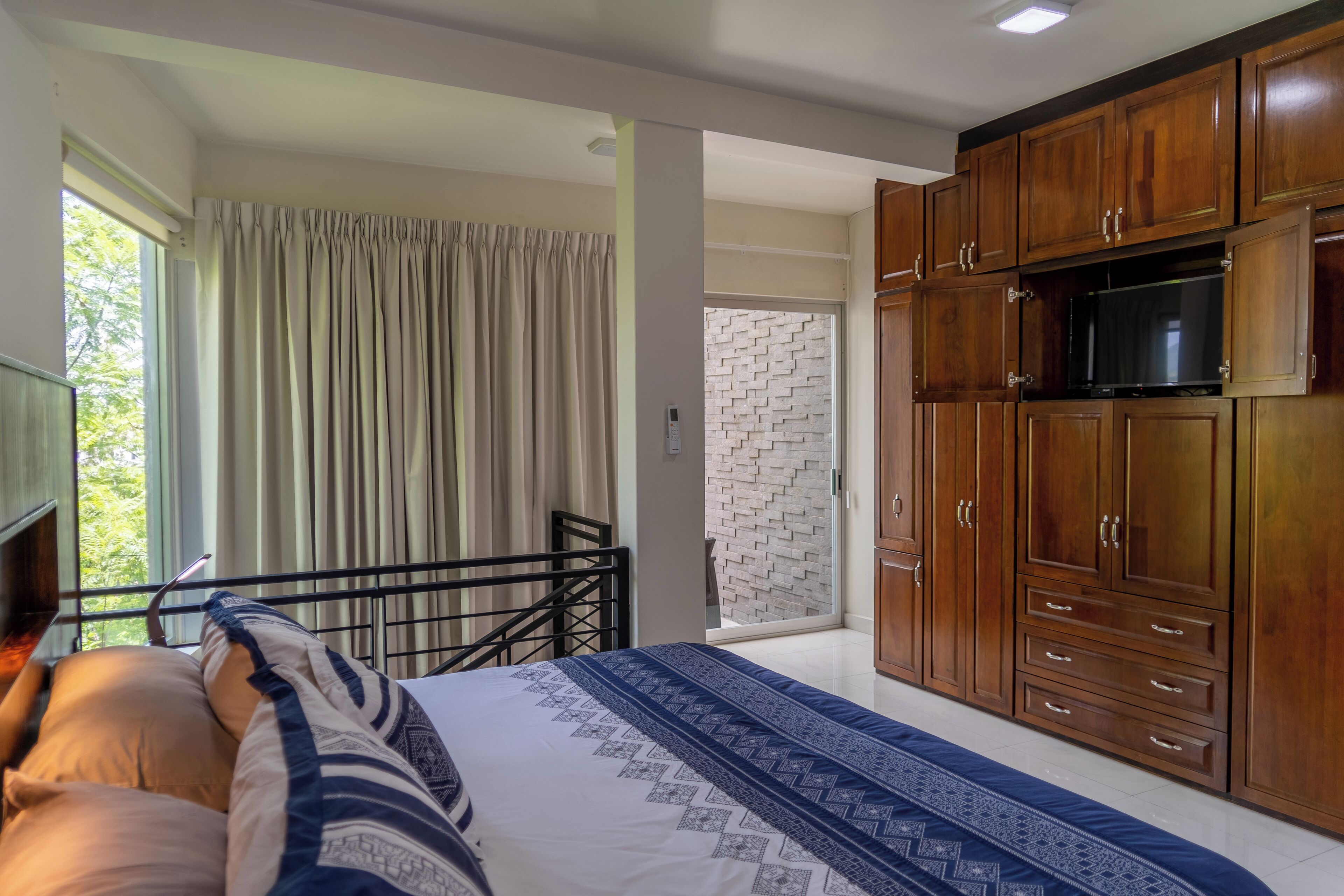 Une chambre à coucher avec un lit, une armoire en bois et un balcon avec des rideaux.