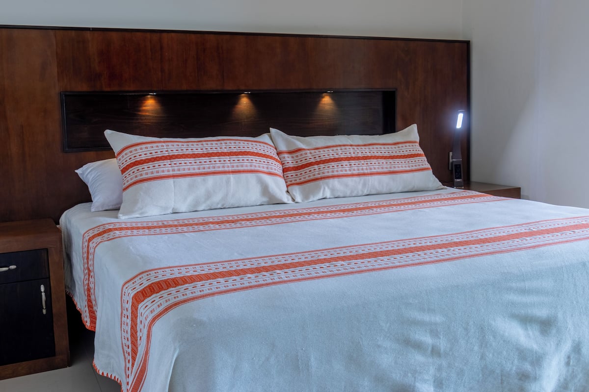 Ein Bett mit weißer Bettwäsche und roten Mustern, ein hölzerner Kopfteil sowie ein Nachttisch mit Schublade.