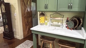 A kitchen with green cabinets, a white countertop, and two stools.