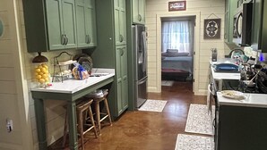 A kitchen with green cabinets, a central island with stools, and a refrigerator.