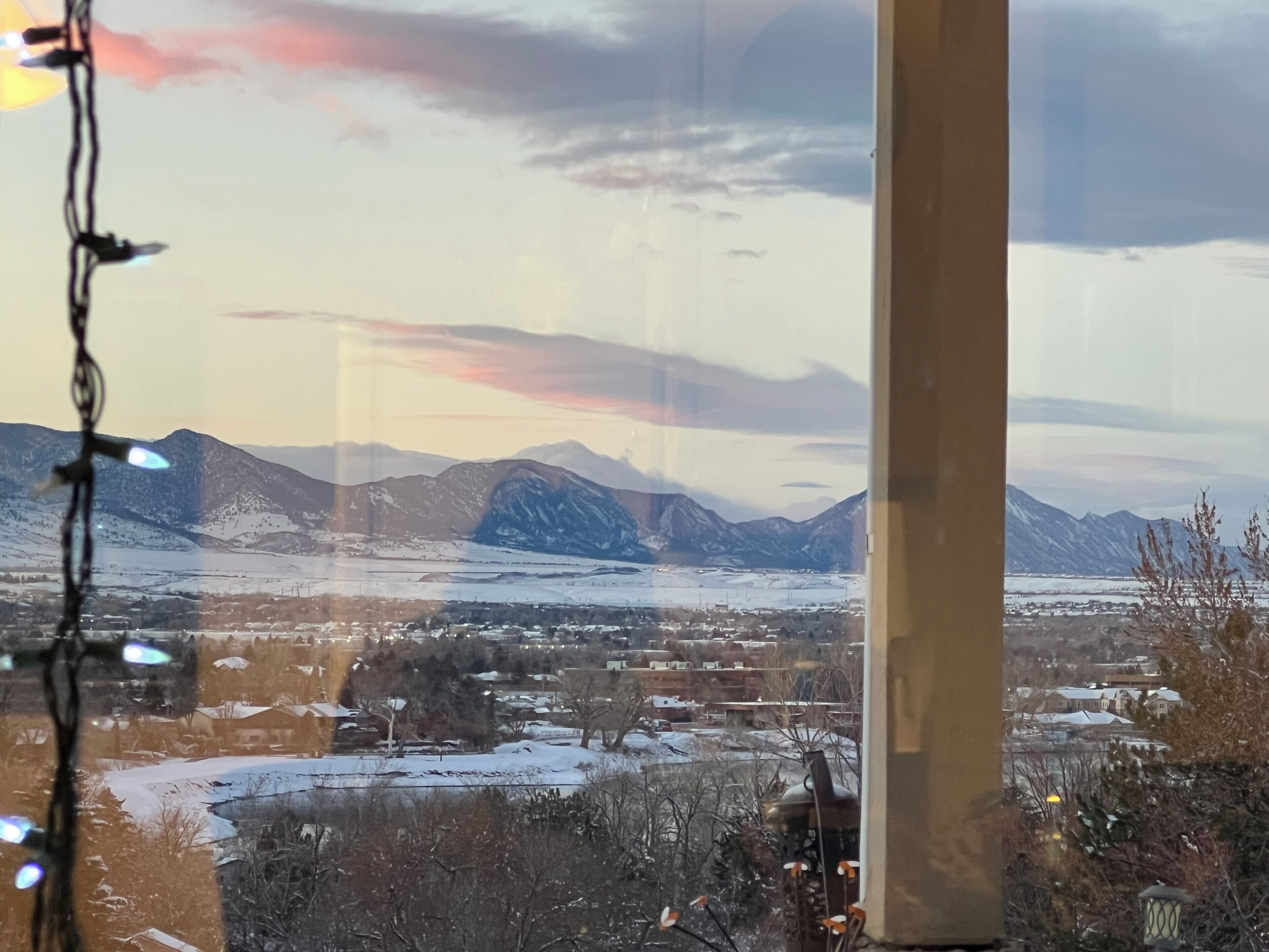 A view of a town with mountains in the background, through a window with string lights.