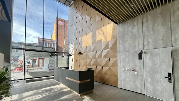 A modern reception area with a wooden reception desk, a geometric patterned wall, and a large window offering a view of the street.