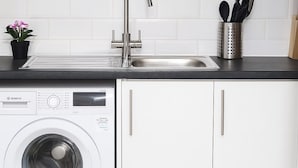 A modern kitchen with a built-in washing machine, a stainless steel sink, and white cabinets.