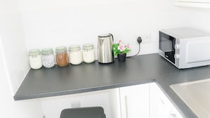 A kitchen with a black countertop, white cabinets, a microwave, a kettle, and jars of food.