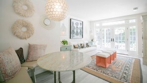 Quarto amplo e iluminado com uma mesa redonda de mármore, um sofá branco e uma grande janela com vista.