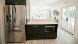 Uma cozinha moderna com geladeira de aço inoxidável, armários pretos, micro-ondas e uma janela grande que traz luz natural.