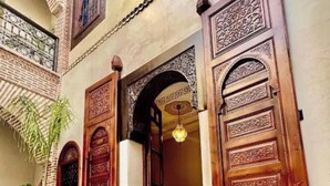 A traditional wooden door with intricate carvings, a hanging light fixture, and a brick wall with a window. - Deluxe Double Room (Marrakech)