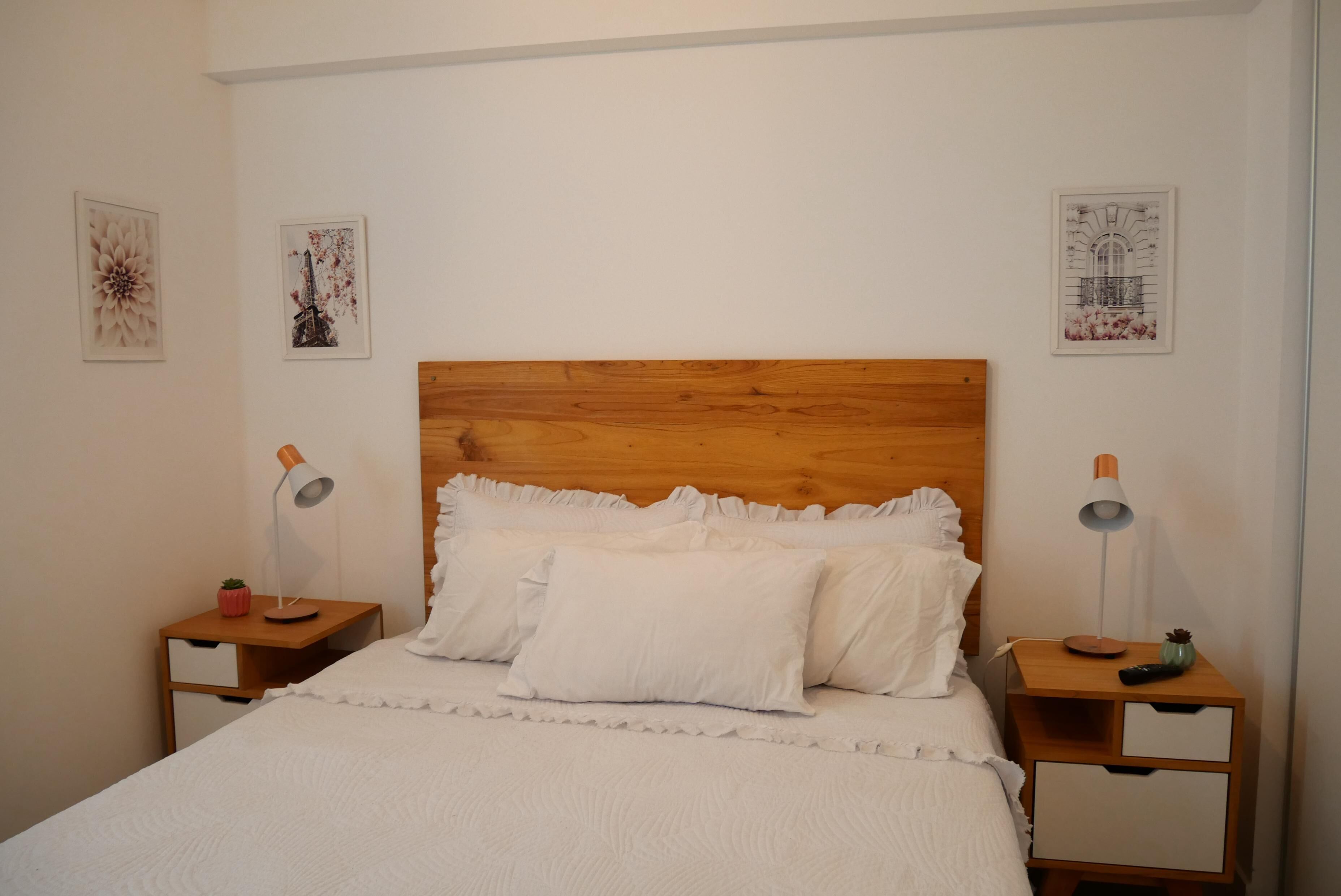 Ein ordentlich eingerichtetes Schlafzimmer mit einem hölzernen Kopfteil, weißer Bettwäsche, zwei Nachttischen mit Lampen und Wanddekoration.