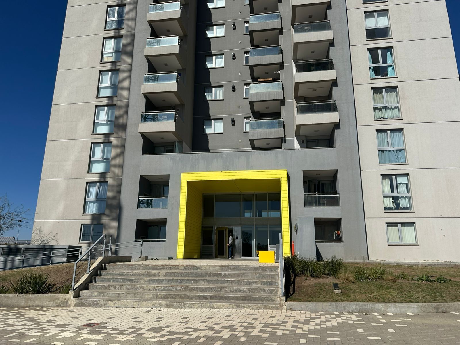 Un edificio moderno de varios pisos con una entrada amarilla destacada y una escalera que lleva a ella.