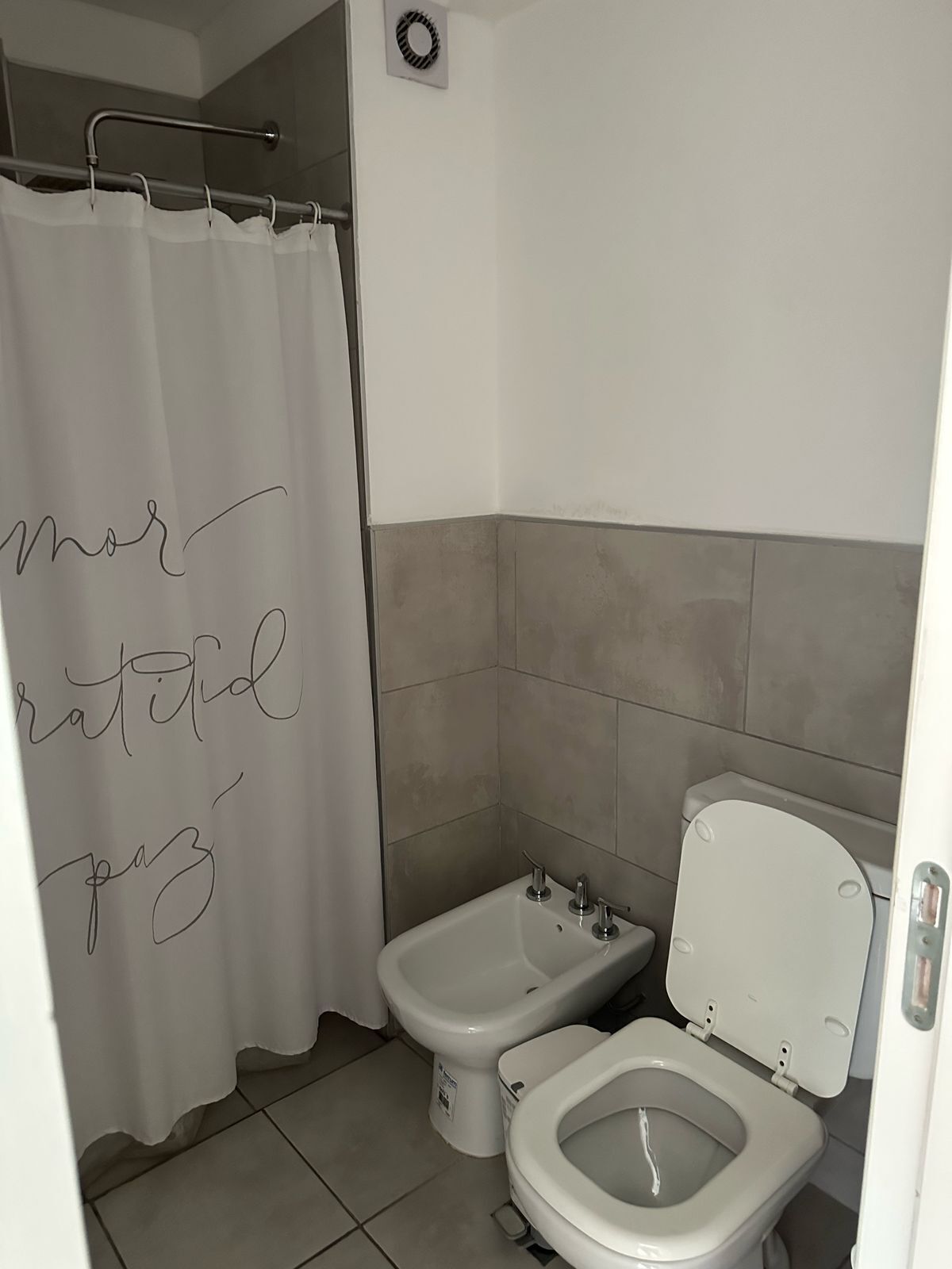 Een badkamer met douchegordijn, een hygiëneschuiver en een toilet.