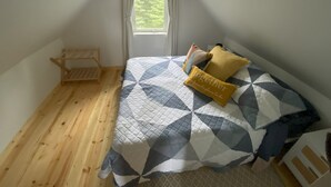 A bedroom with a wooden floor, a bed with a geometric patterned bedspread, two pillows, and a small wooden shelf. - Rustic Homer Cabin w/ Moose Views & Quiet Porch (Homer)