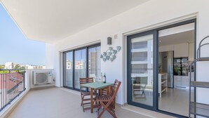 Un balcon avec une table et des chaises, une porte-fenêtre coulissante donnant sur une cuisine et une vue sur la ville.