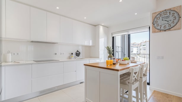 Une cuisine moderne avec des meubles blancs, un îlot central en bois et une grande fenêtre.
