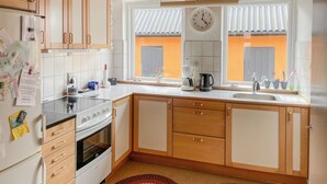 A kitchen with wooden cabinets, a stove, a sink, and a window with a clock.