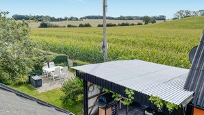 A patio area with a metal roof, a table and chairs, and a view of a cornfield.