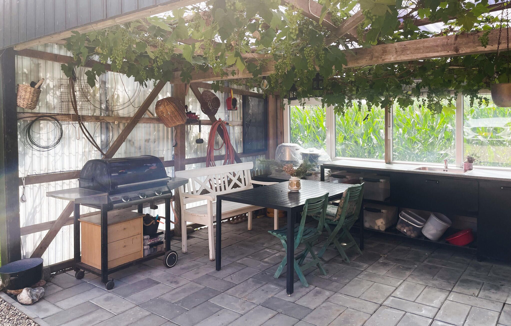 En overdækket terrasse med grill, et bord og stole.