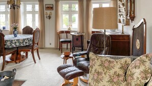 A traditional room with a dining table, chairs, a sofa, a lamp, and a bookshelf.
