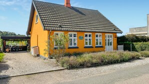 A yellow house with a tiled roof, a small garden, and a gravel driveway.