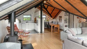 A spacious loft with a high ceiling, wooden beams, a kitchen with white cabinets, a dining area with a wooden table and chairs, and a grey sofa. - Awesome home in Tranekær with WiFi (Tranekær)