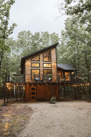 Une cabane moderne en bois, dotée de grandes fenêtres, d’une terrasse et d’un éclairage extérieur.