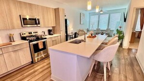 Cozinha moderna com armários de madeira, eletrodomésticos de aço inoxidável e uma ilha central com banquetas.