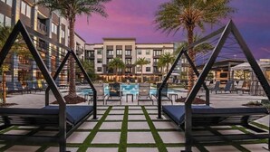 Área de piscina de hotel com espreguiçadeiras, mesa de bilhar e um edifício ao fundo.