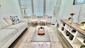 Uma sala de estar moderna com sofá, duas poltronas, mesa de centro, luminária de chão, espelho e estante de madeira com plantas.